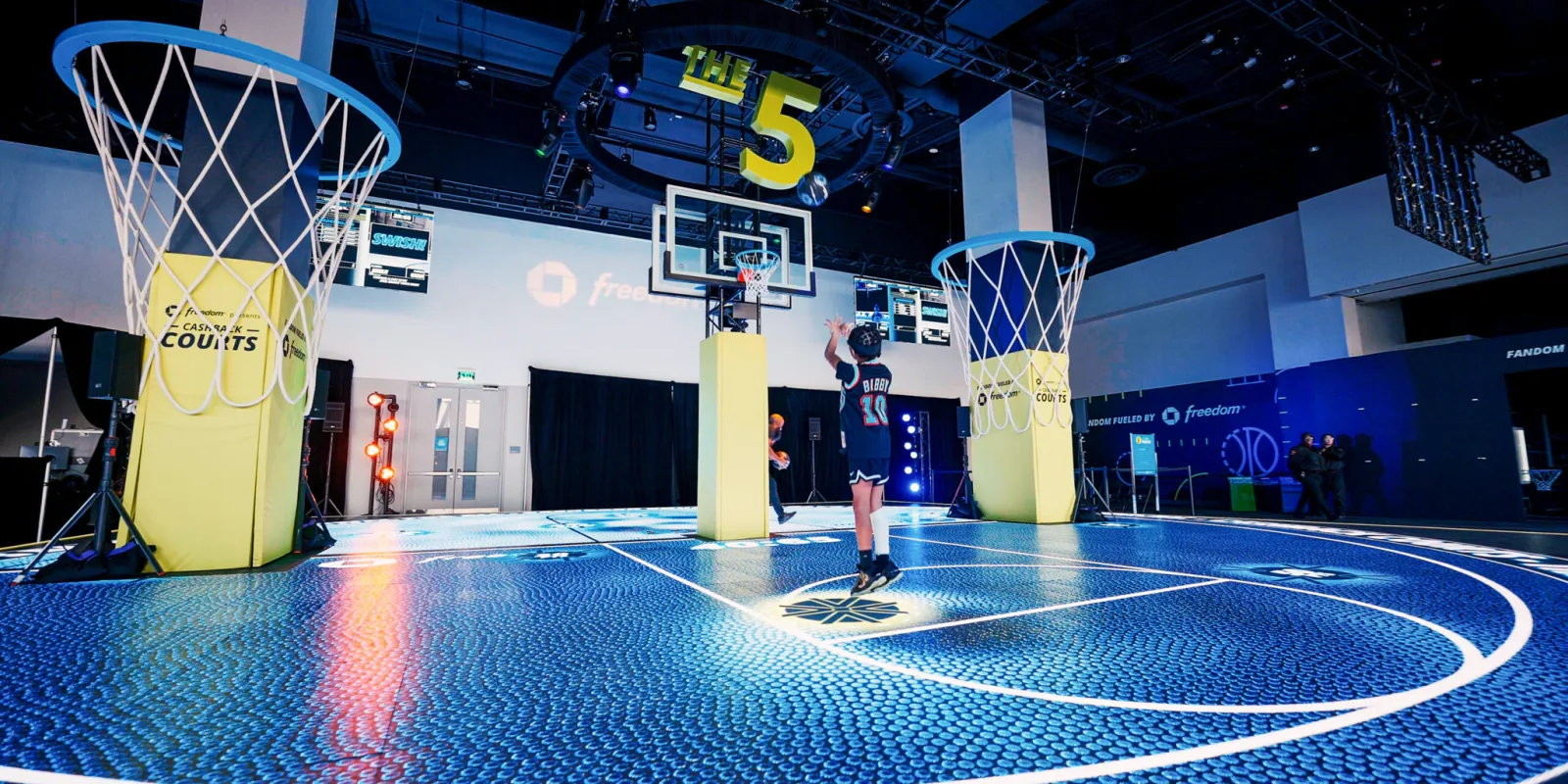 A participant plays on a blue illuminated interactive basketball court beneath a central hoop.