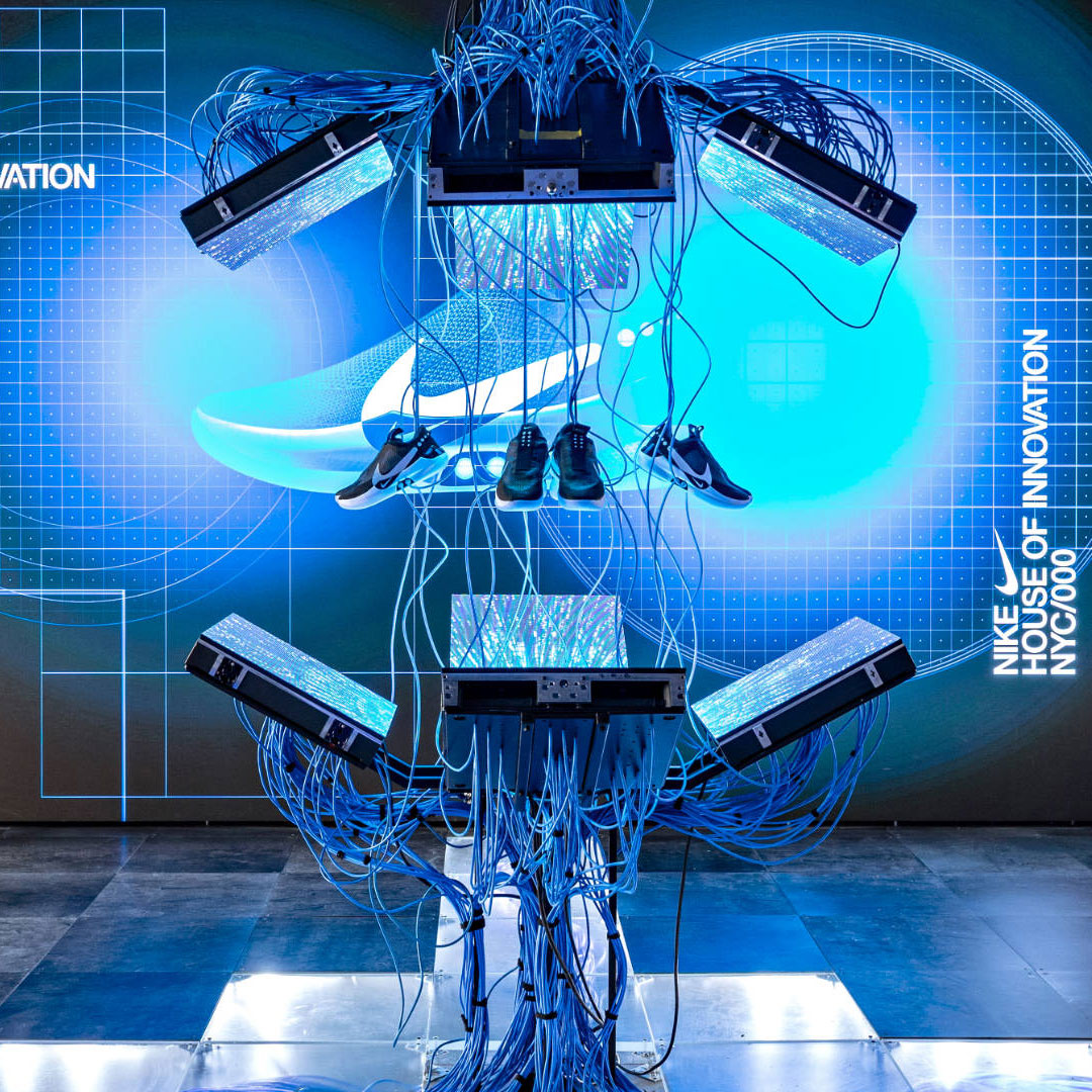 A suspended shoe display and mechanical structure in front of bright blue Nike imagery.
