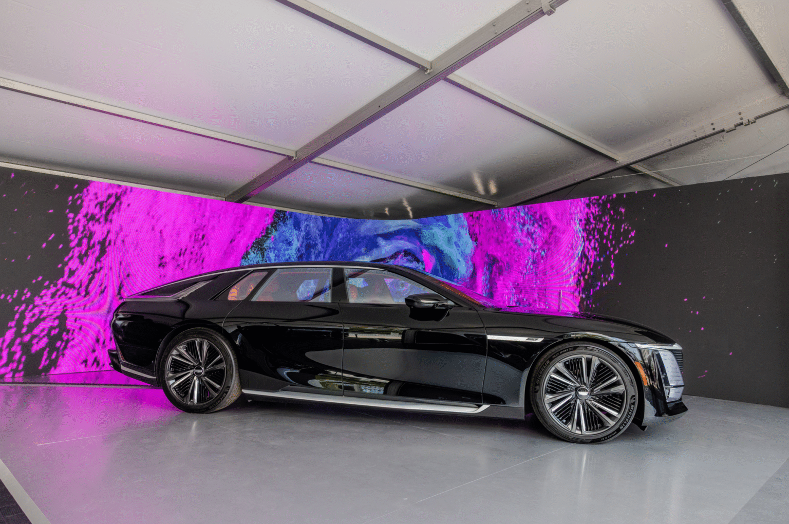 A black Cadillac displayed in front of a curved screen showing pink and blue graphics.