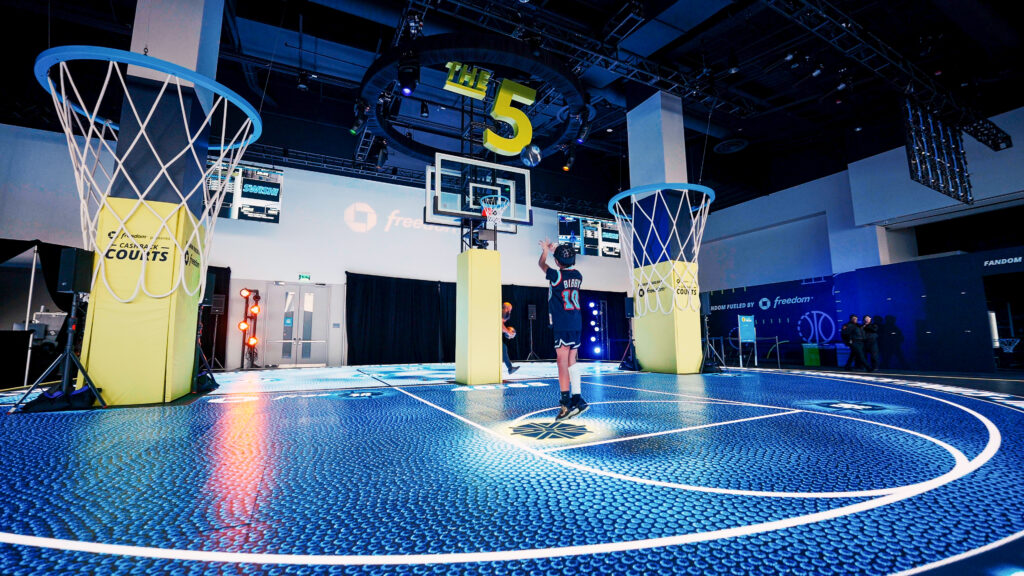 A player shoots toward a hoop on the illuminated blue Chase basketball court.
