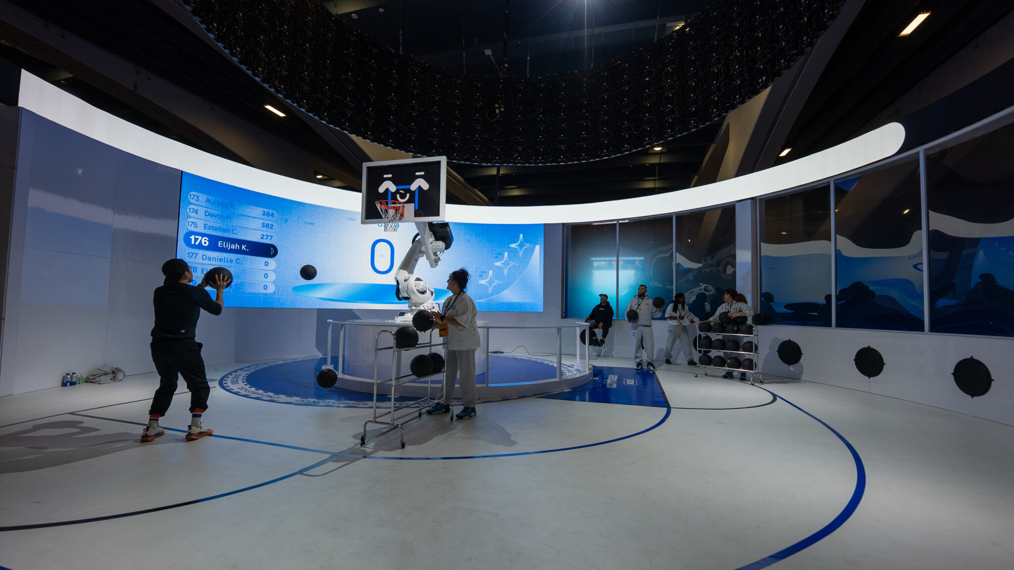 A basketball hoop mounted on a robotic arm in front of a curved blue display at Coinbase ASW.