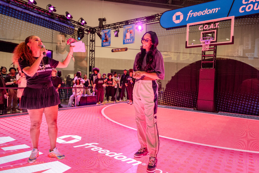 Two presenters speak on the pink-lit Chase basketball court.