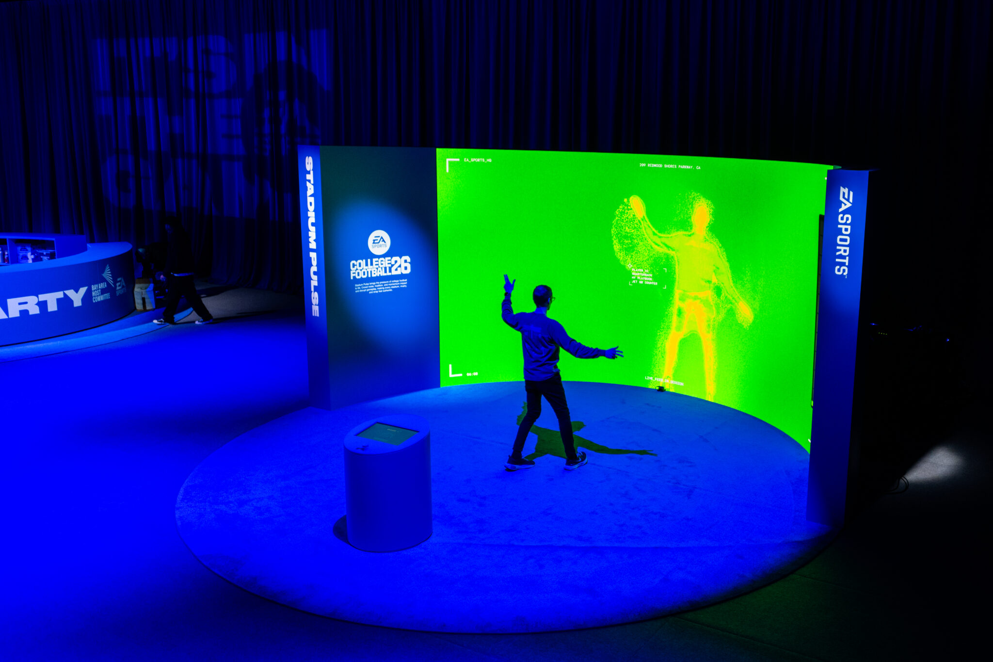 A visitor raises their arms in front of a green silhouette on a curved EA Sports display.