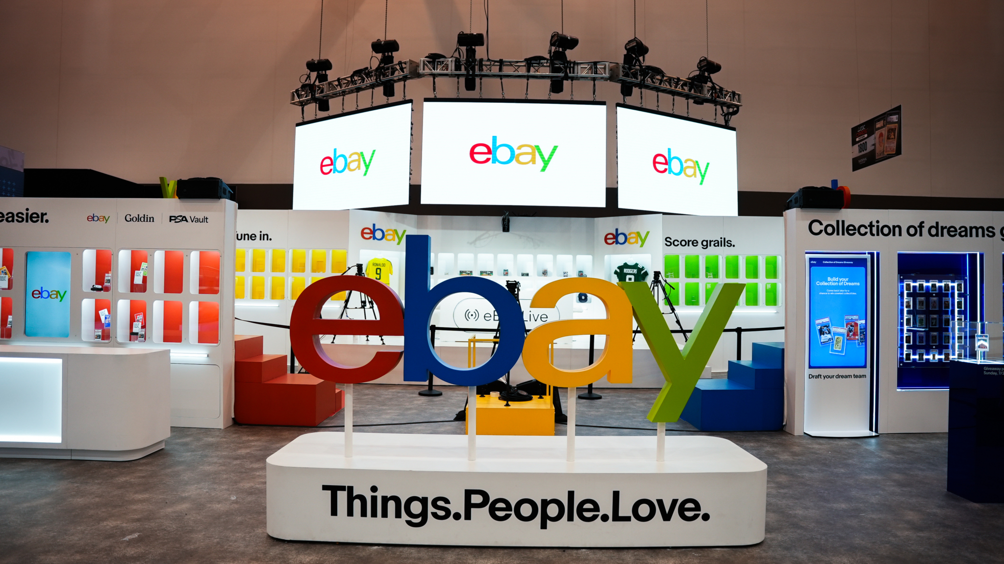 Large multicolored eBay letters beneath a suspended display in an exhibition booth.