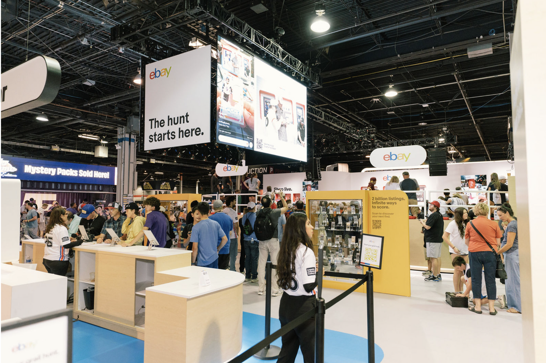 Visitors gather around the eBay Live exhibit beneath a suspended video display.