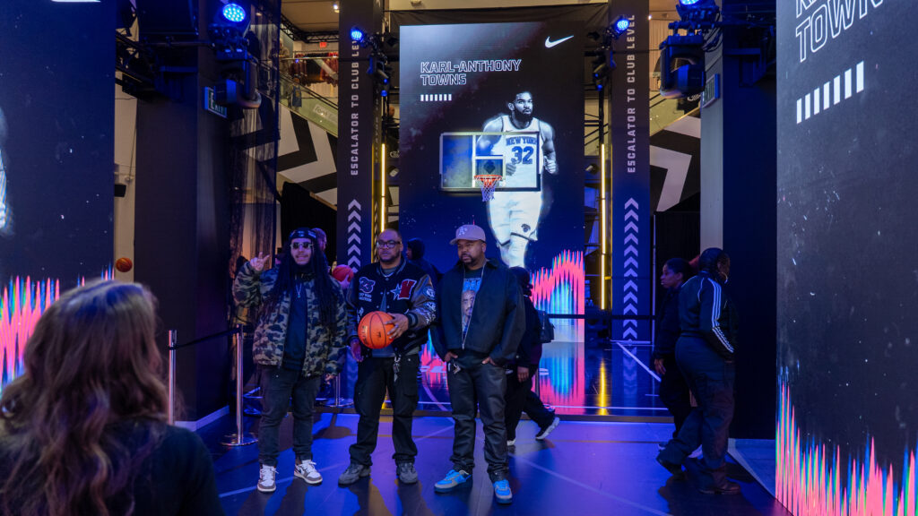 Visitors pose in front of a tall basketball display at Foot Locker ASW.