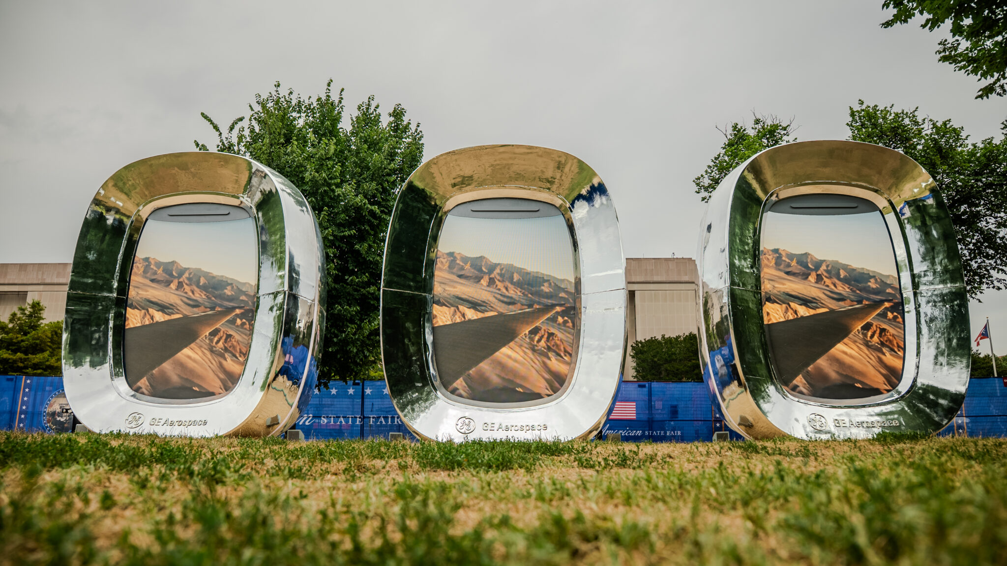 Three aircraft-style windows show landscape imagery in the outdoor GE exhibit.