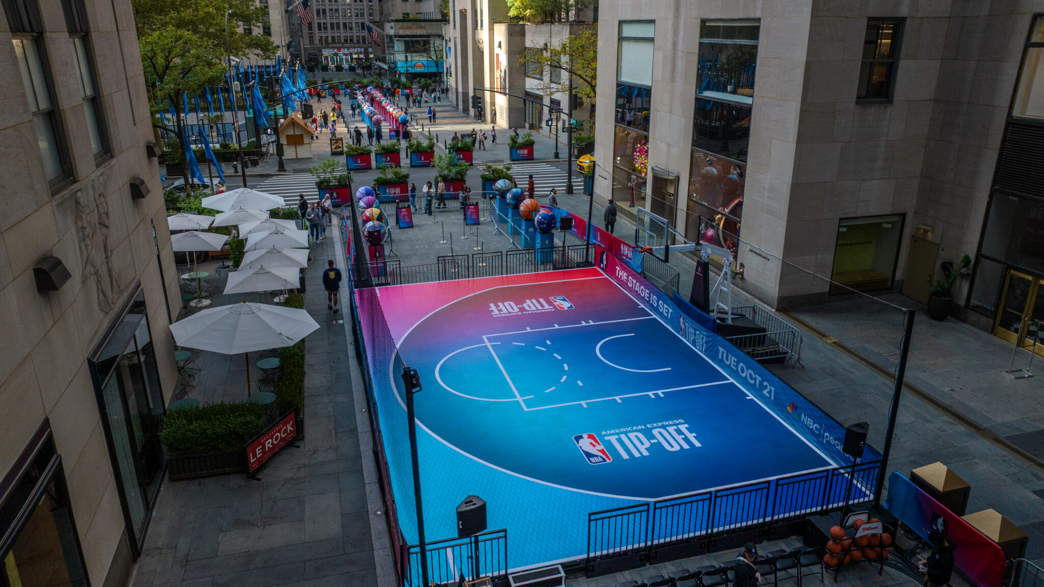 A blue and pink basketball court with NBA on NBC branding between buildings at Rockefeller Center.