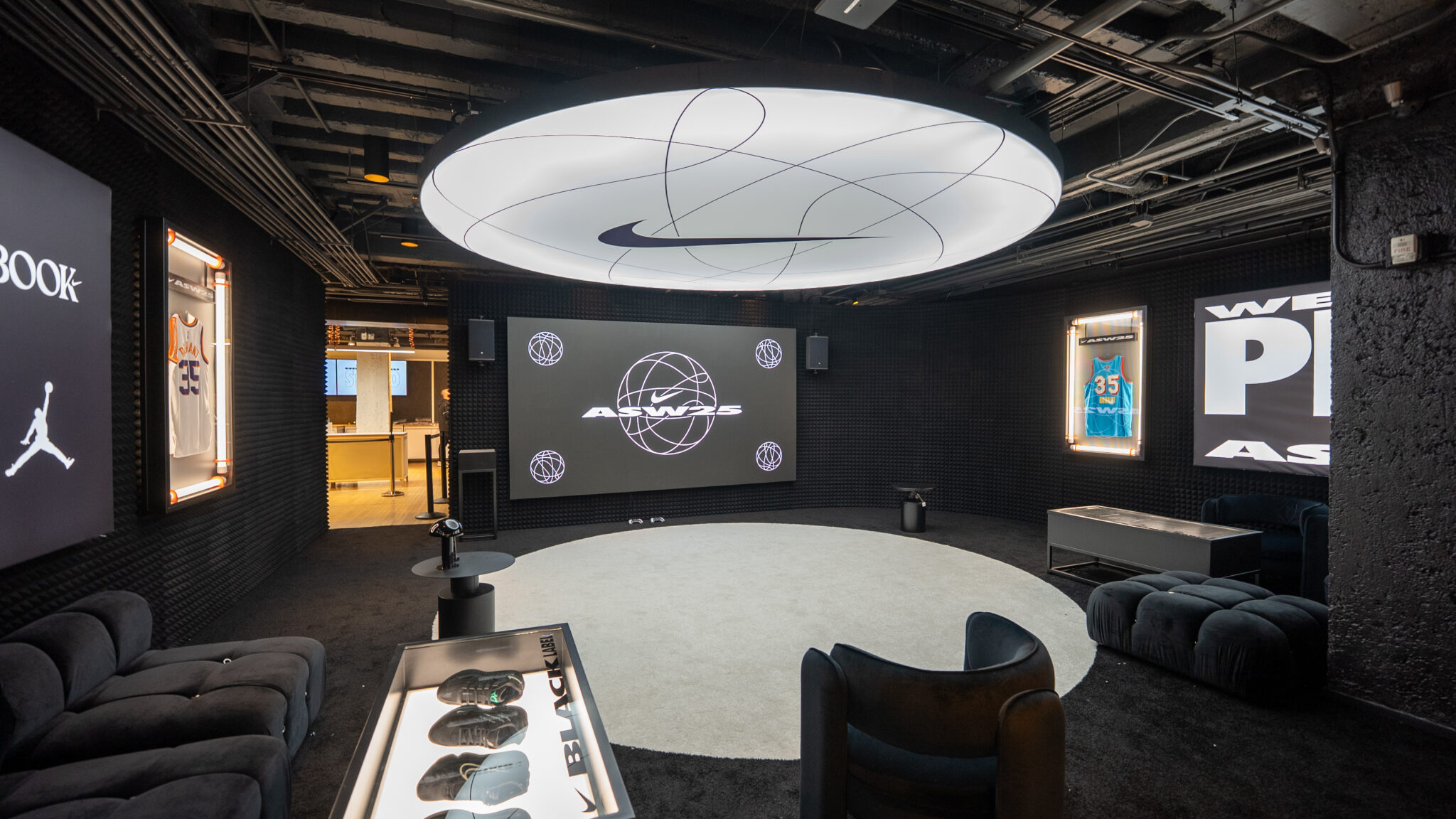 Dark lounge seating and basketball graphics beneath a circular light in the Nike NBA2K lounge.