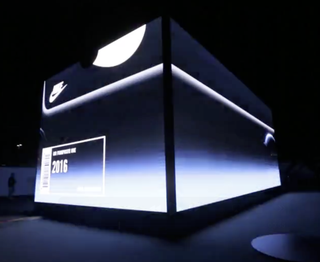 A large black Nike SNKRS Box outlined with illuminated edges at night.