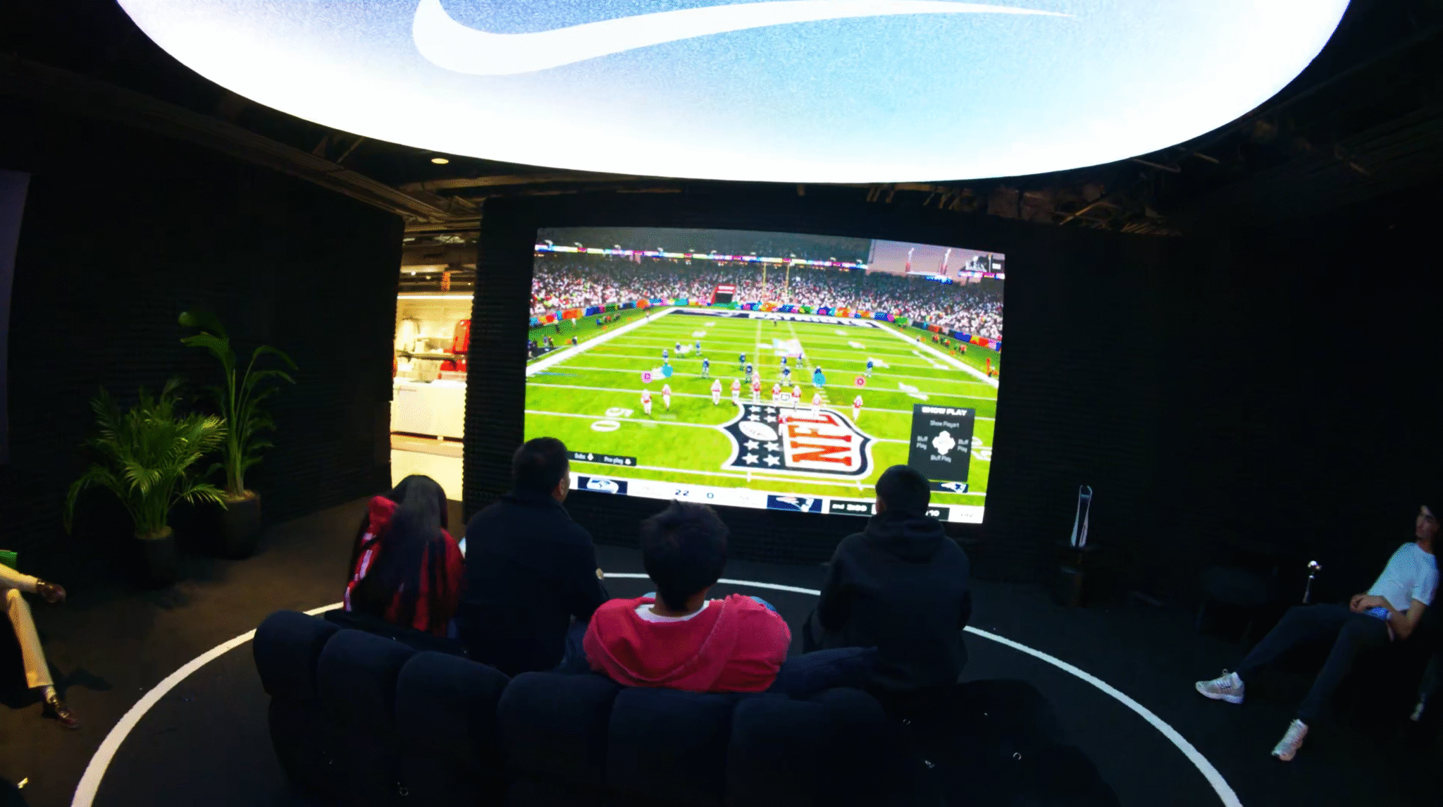 Visitors watch football on a large screen beneath a circular ceiling light in the Nike lounge.