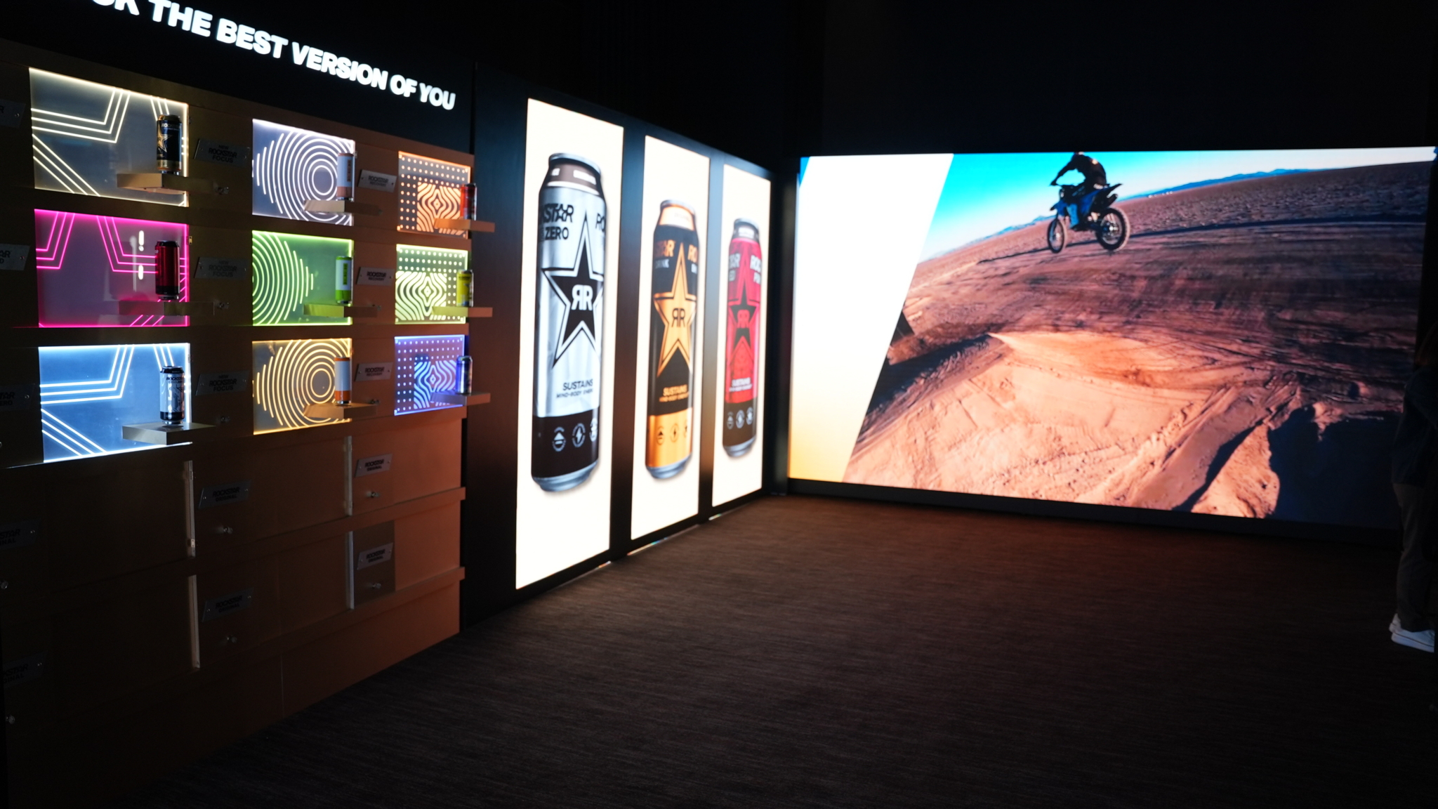 A large video wall beside product displays at the Rockstar activation.